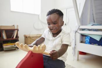 Young Boy Sitting On Ride On Toy In Playroom