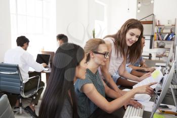 Three women working together at computer in open plan office