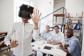Woman wearing VR goggles watched by colleagues in an office