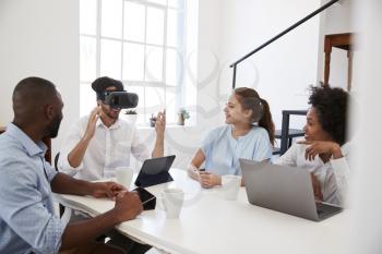 Man in VR goggles at a desk watched by colleagues in office