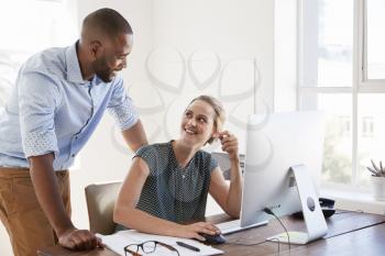 Man stands talking to woman smiling at her desk in an office