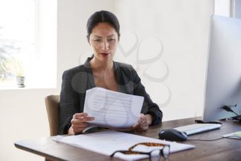 Young Asian woman reading documents at her desk in an office