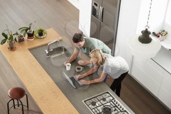 Overhead View Of Couple Looking At Laptop In Modern Kitchen