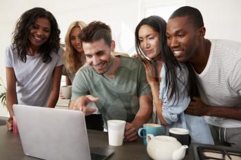 Friends Looking At Laptop And Drinking Coffee In Modern Kitchen