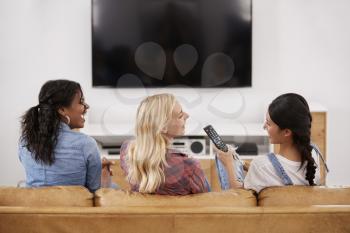 Rear View Of Female Friends Sitting On Sofa Watching Television