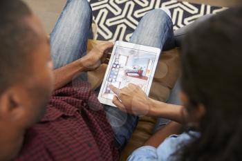 Couple Sitting On Sofa Looking At Home Improvement App