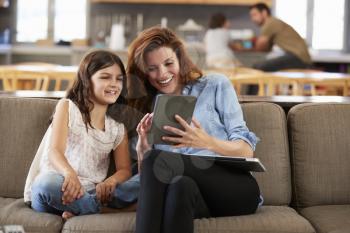 Mother And Daughter Sitting On Lounge Sofa Using Digital Devices