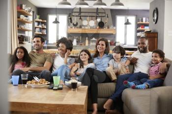 Two Families Sitting On Sofa Watching Television Together