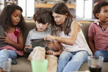 Group Of Children Sitting On Sofa Using Digital Devices