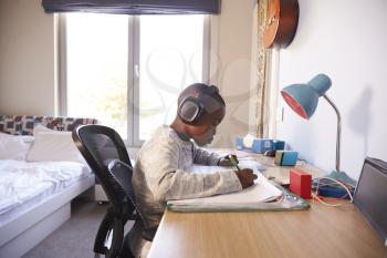 Young Boy In Bedroom Wearing Headphones And Doing Homework
