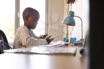 Boy In Bedroom Using Digital Tablet To Do Homework