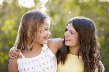 Portrait of two smiling young girls looking at each other outdoors