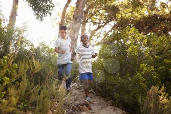 Two smiling young boys running down a forest path
