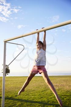 Smiling girl having fun hanging from a goal post