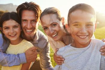 Portrait of happy white family embracing outdoors, backlit