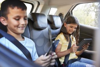Boy and girl in a car using tablets during family road trip