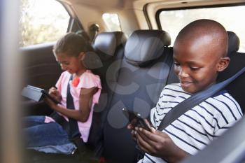 Boy and girl in a car using tablet and smartphone on a trip