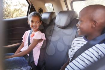 Smiling girl and boy looking at each other in car on a trip
