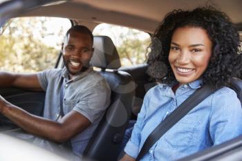 Happy young black couple driving in a car smiling to camera