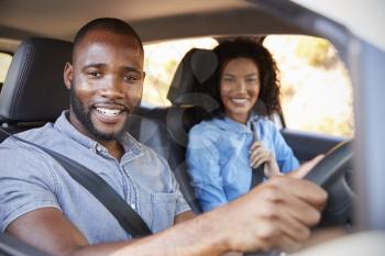 Young black couple in a car on a road trip smiling to camera
