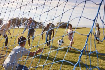 Two families playing football in park seen through goal net
