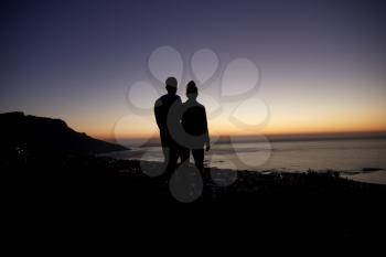 Couple strolling by the sea at sunset on a beach, silhouette