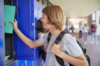 White teenage schoolboy using locker in school corridor