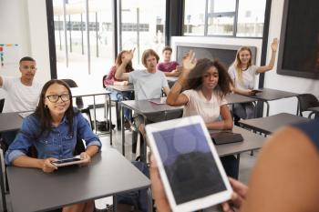 Teacher uses tablet in high school class, over shoulder view