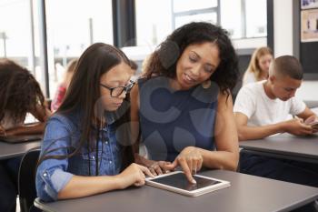 Teacher helping teenage schoolgirl with tablet computer