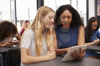 Teacher helps blonde teenage schoolgirl with tablet computer