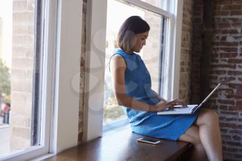 Businesswoman In Office Sitting By Window Using Laptop