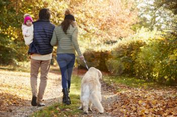 Family With Daughter And Dog Enjoy Autumn Countryside Walk