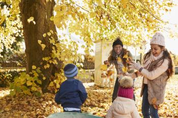 Children Helping Mother To Collect Autumn Leaves In Garden