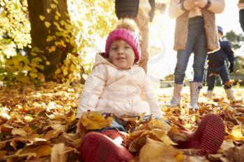 Young Girl Sitting In Leaves In Autumn Garden