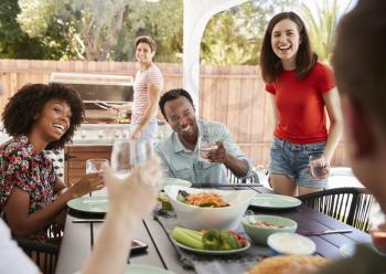 Young adult friends sitting outdoors for lunchtime barbecue