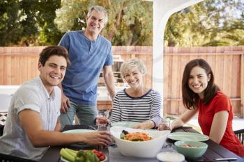 Parents and adult children at table in garden look to camera