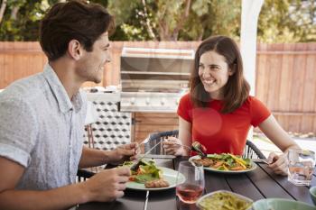 Young white couple eating lunch at a table in the garden
