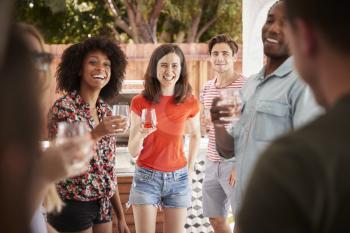 Young adult friends standing with drinks at a backyard party