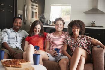 Four young adult friends relaxing on couch together at home