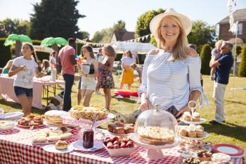 Portrait Of Mature Woman Serving On Cake Stall At Busy Summer Garden Fete