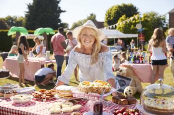 Portrait Of Mature Woman Serving On Cake Stall At Busy Summer Garden Fete