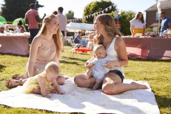 Two Mothers With Babies On Rug At Summer Garden Fete