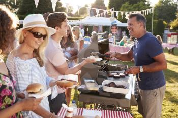 Man Serving On Barbeque Stall At Summer Garden Fete