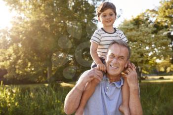 Portrait Of Grandfather Giving Grandson Ride On Shoulders In Summer Park