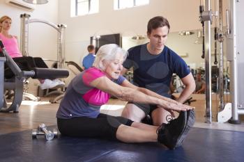 Senior Woman Exercising In Gym Being Encouraged By Personal Trainer