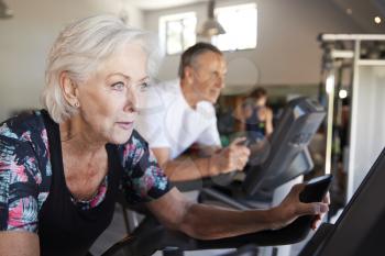 Active Senior Couple Exercising On Cycling Machines In Gym