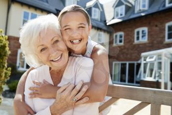 Portrait Of Granddaughter Hugging Grandmother On Bench During Visit To Retirement Home