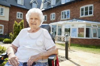 Portrait Of Senior Woman Sitting Outside Retirement Home In Motorized Wheelchair