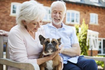 Retired Couple Sitting On Bench With Pet French Bulldog In Assisted Living Facility