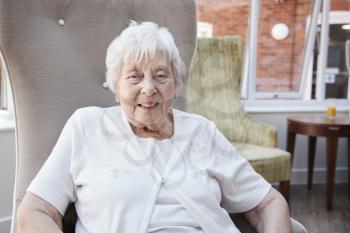 Portrait Of Senior Woman Sitting In Chair In Lounge Of Retirement Home